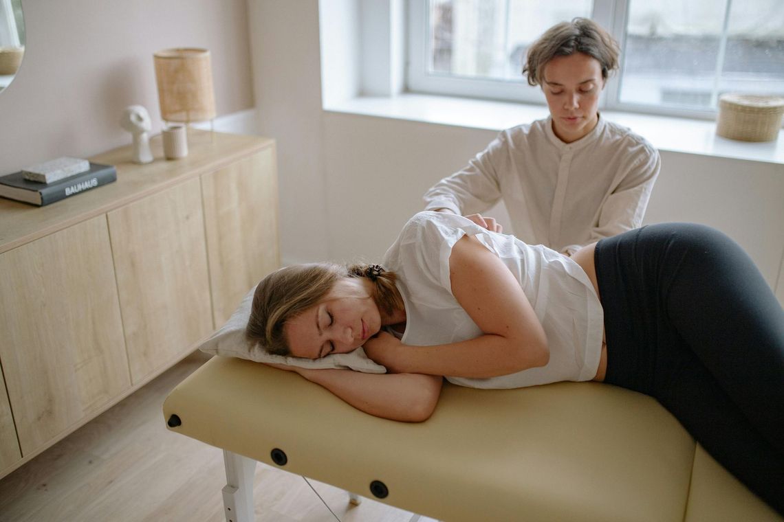 Woman getting a massage from a practitioner; indoors, white top, beige table.