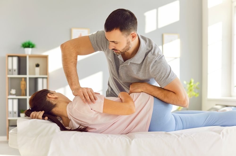 Chiropractor adjusting a woman's back on a couch in a bright room.