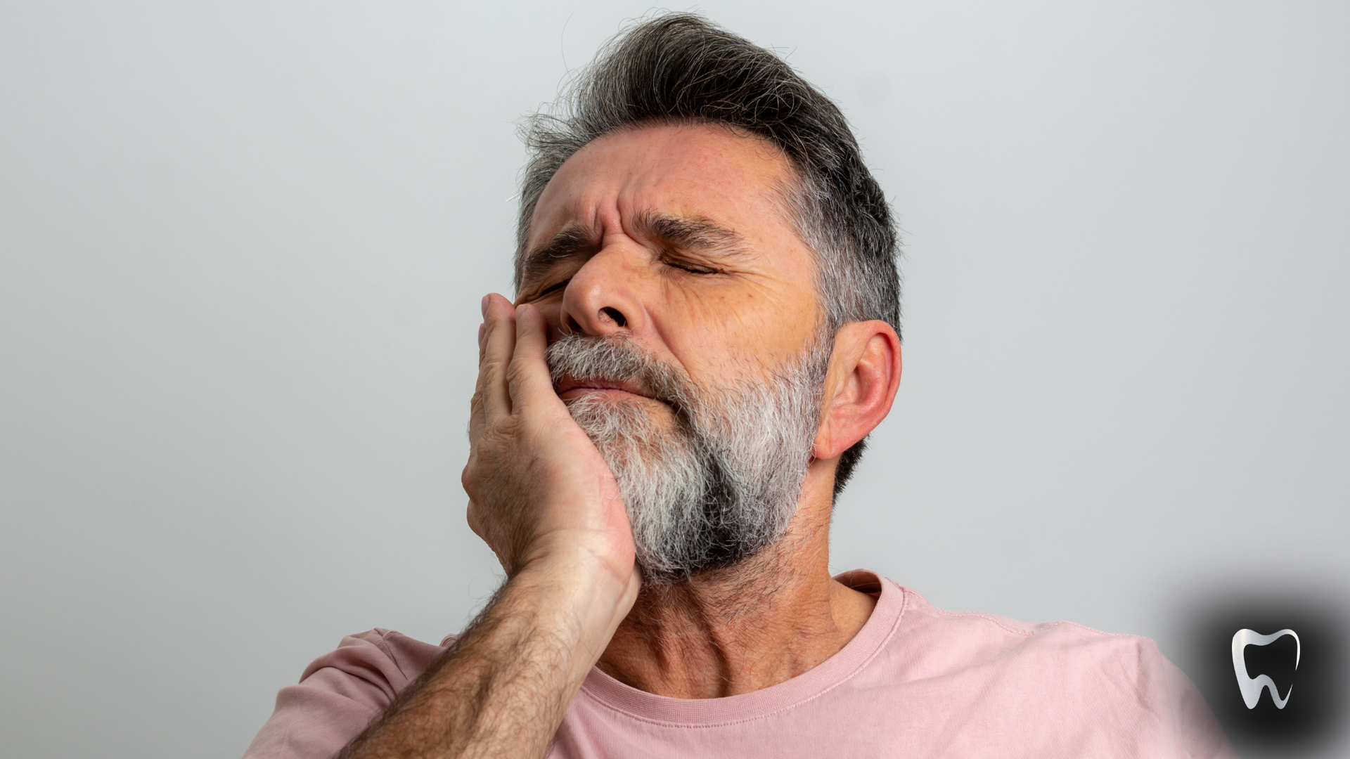 Man with closed eyes holding his cheek, appearing to be in pain.