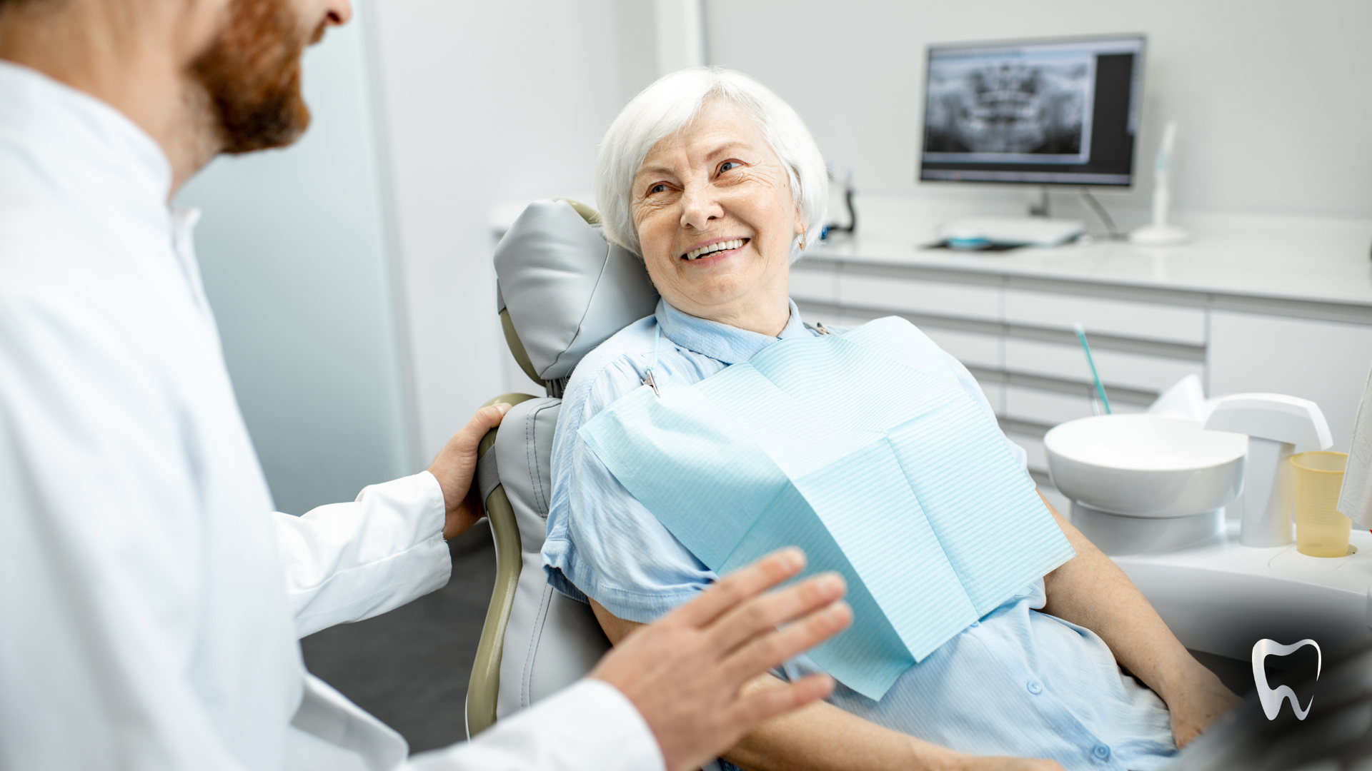 An elderly woman is sitting in a dental chair talking to a dentist.