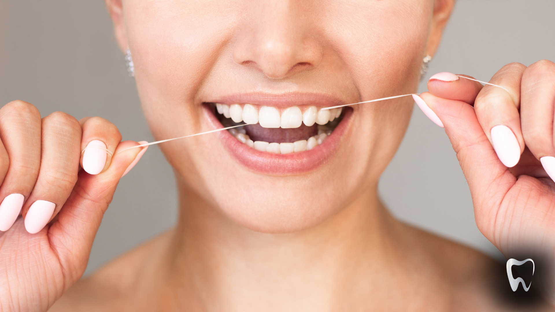 Woman flossing her teeth, smiling, with bright white teeth and light pink nail polish.