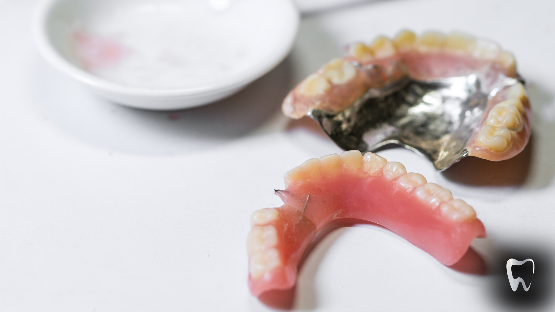 A broken denture is sitting on a white surface next to a bowl.