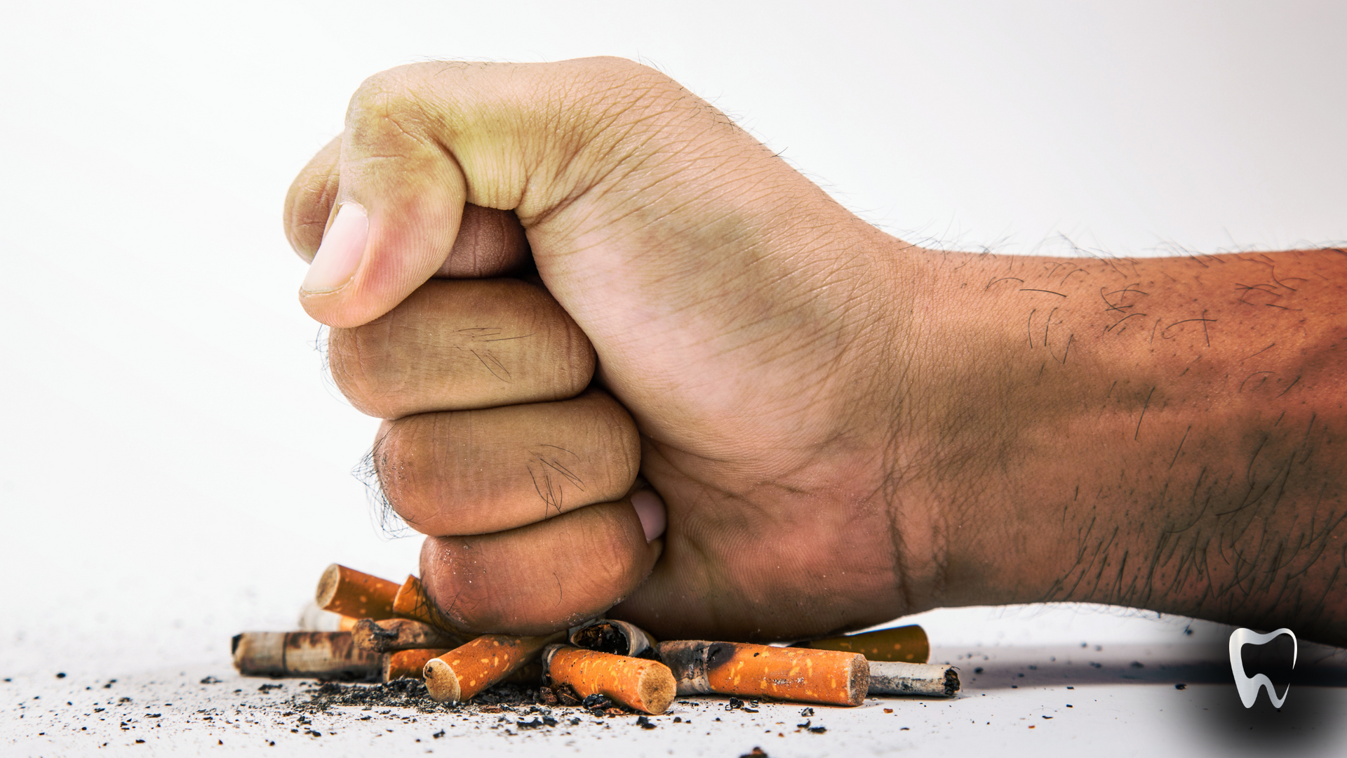A person is holding a fist over a pile of cigarettes.