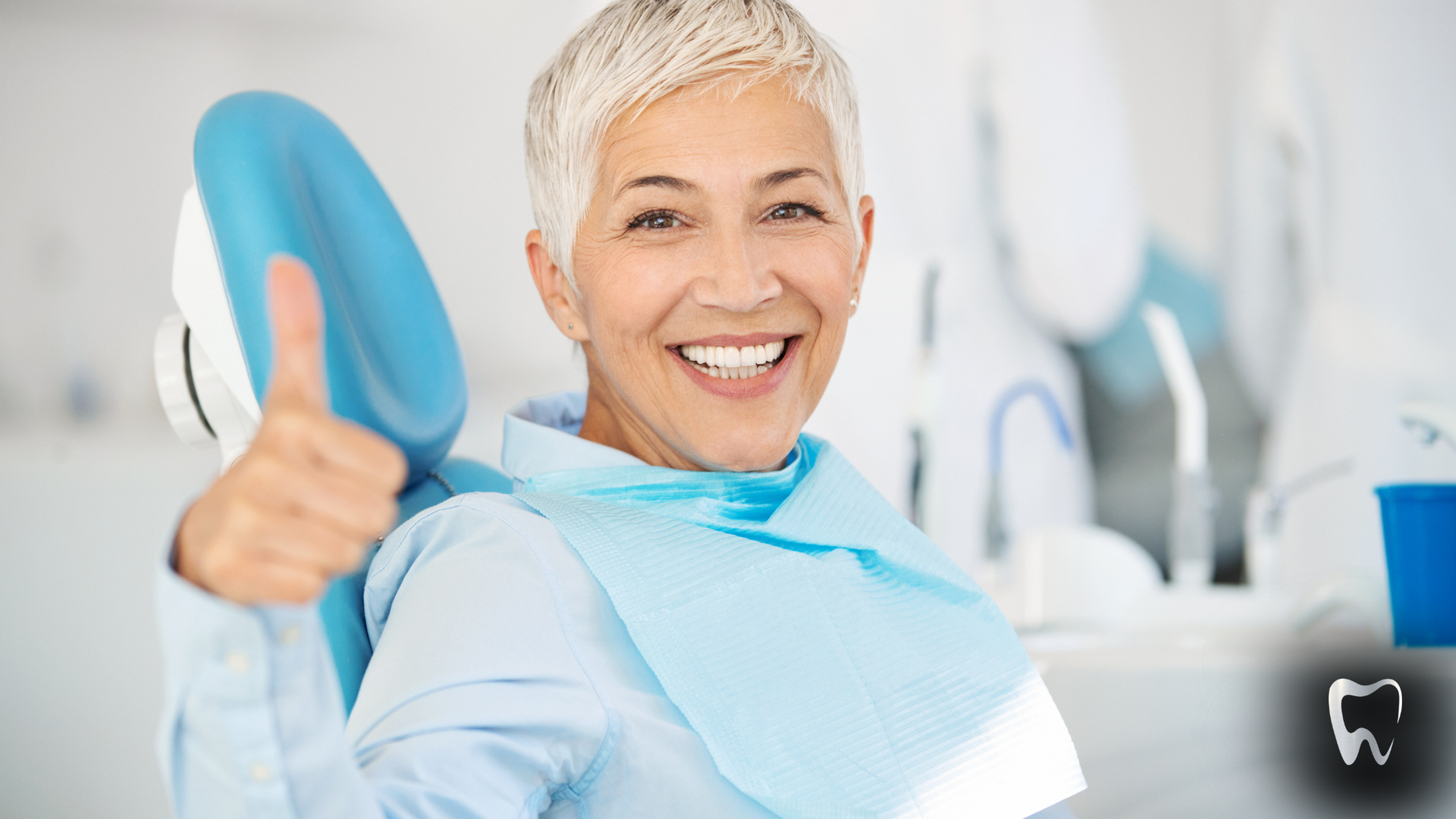 A woman is sitting in a dental chair giving a thumbs up.