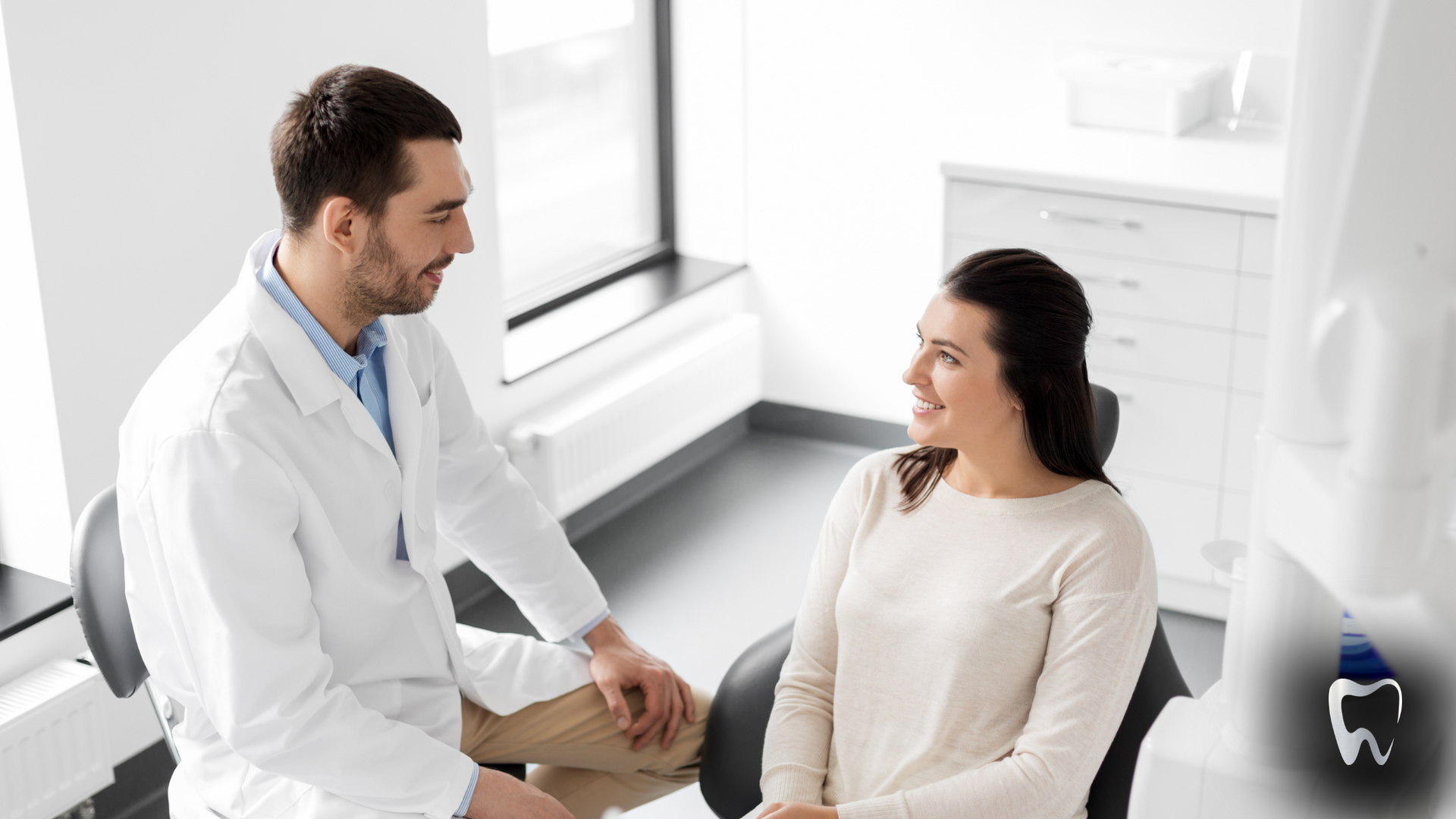 A dentist is talking to a woman in a dental chair.
