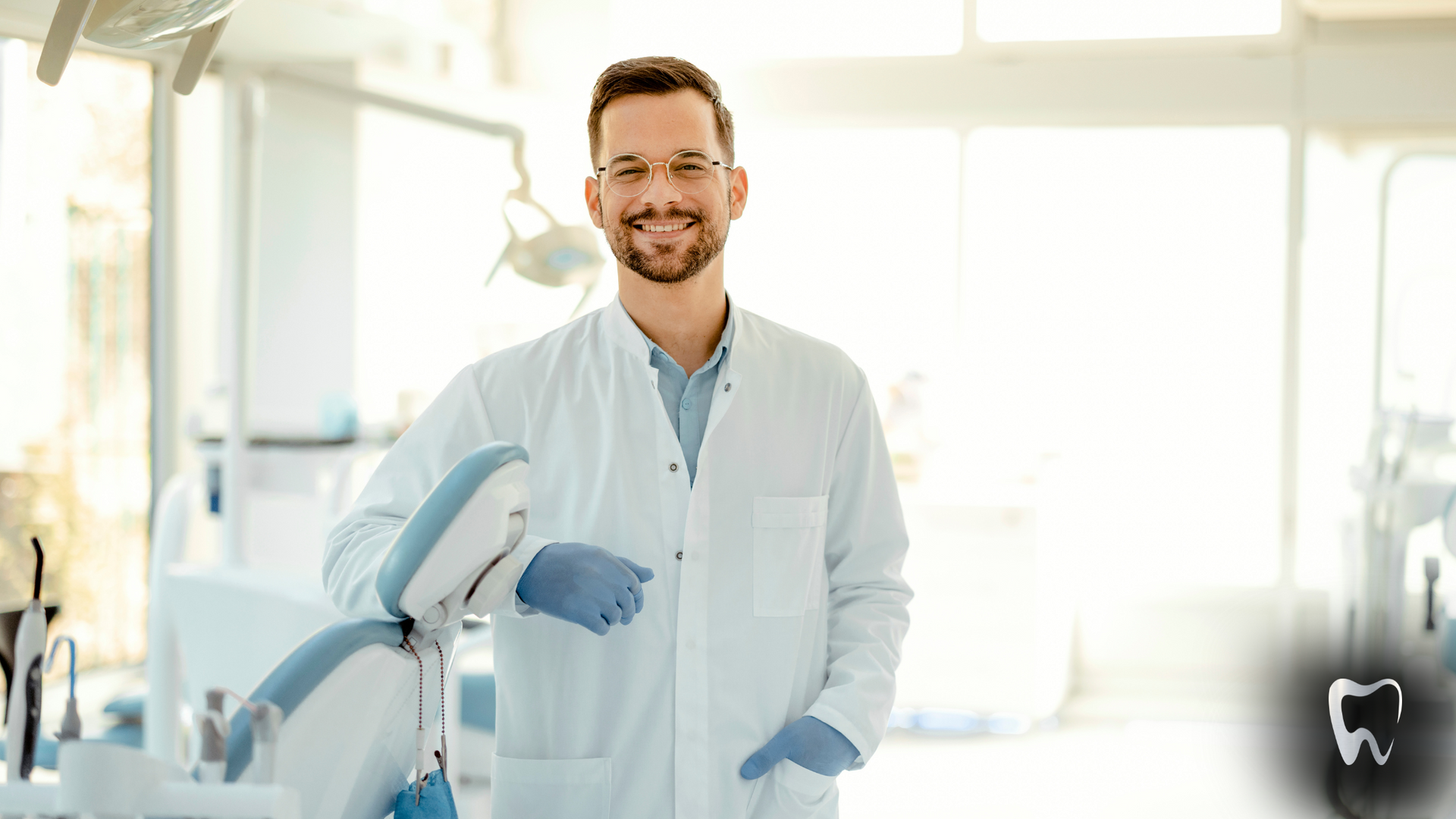 A dentist is smiling while holding a machine in a dental office.