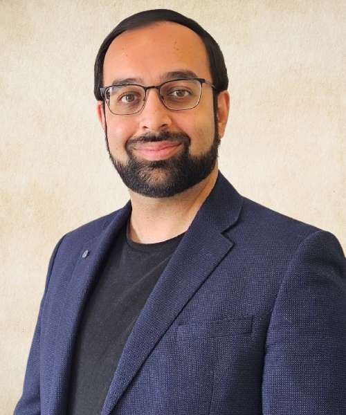 A man with a beard wearing glasses and a blue jacket