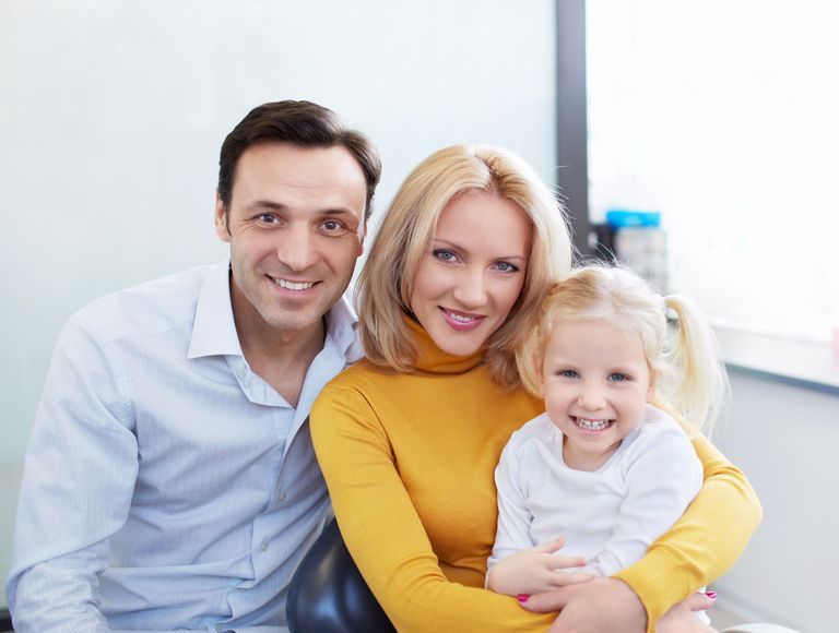 Woman in dental chair smiles at dentist with clipboard.