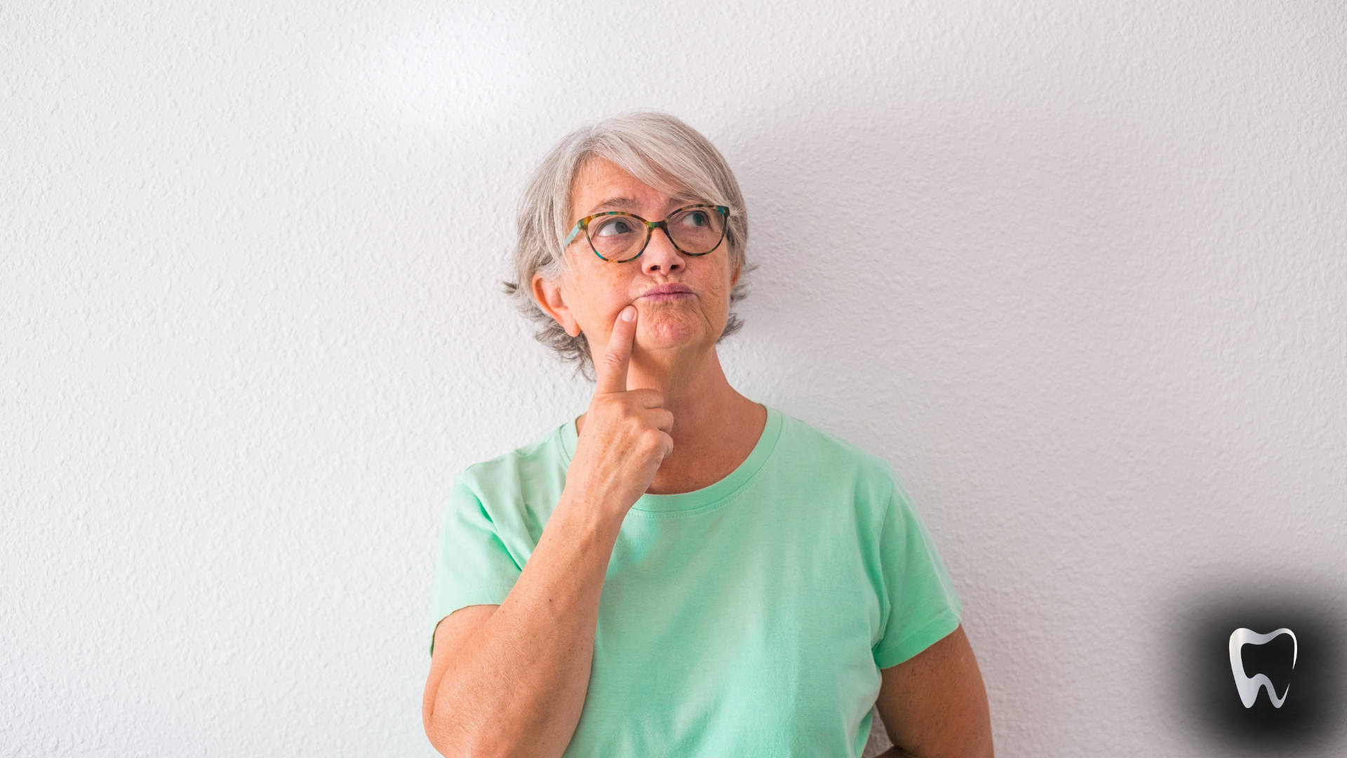 An elderly woman wearing glasses and a green shirt is thinking.