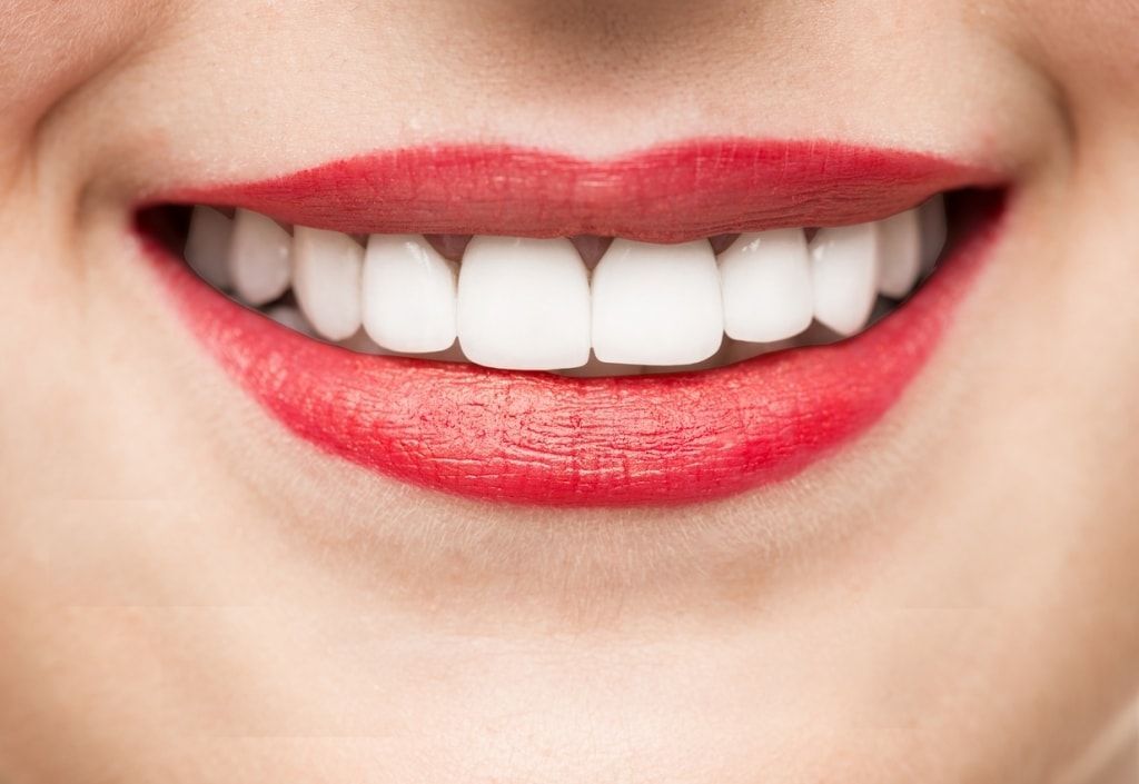 A close up of a woman 's mouth with red lipstick and white teeth.