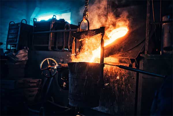A large bucket of molten metal is being poured into a furnace.