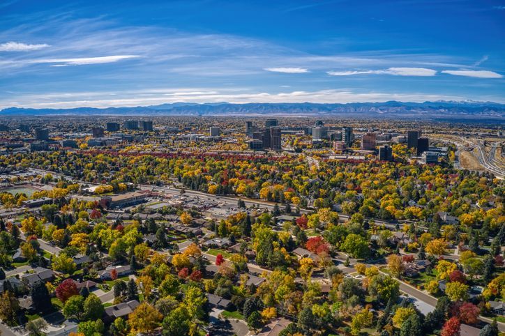 An aerial view of Denver Co with trees in the foreground and mountains in the background.