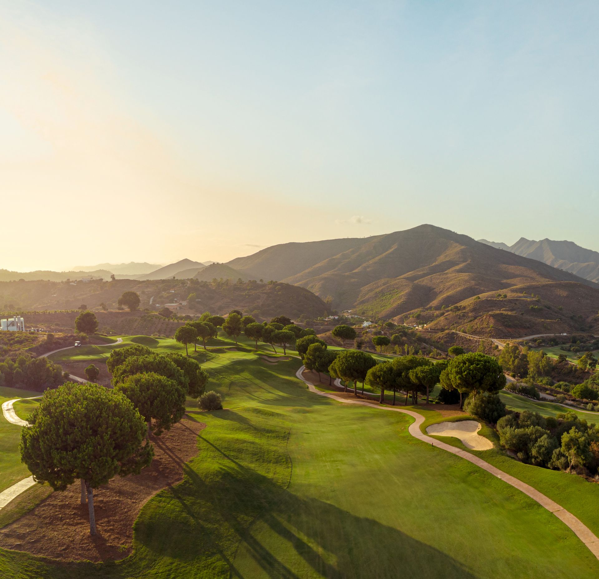 Parcours de golf ensoleillé, avec des allées verdoyantes, des arbres et des montagnes ondulantes en arrière-plan