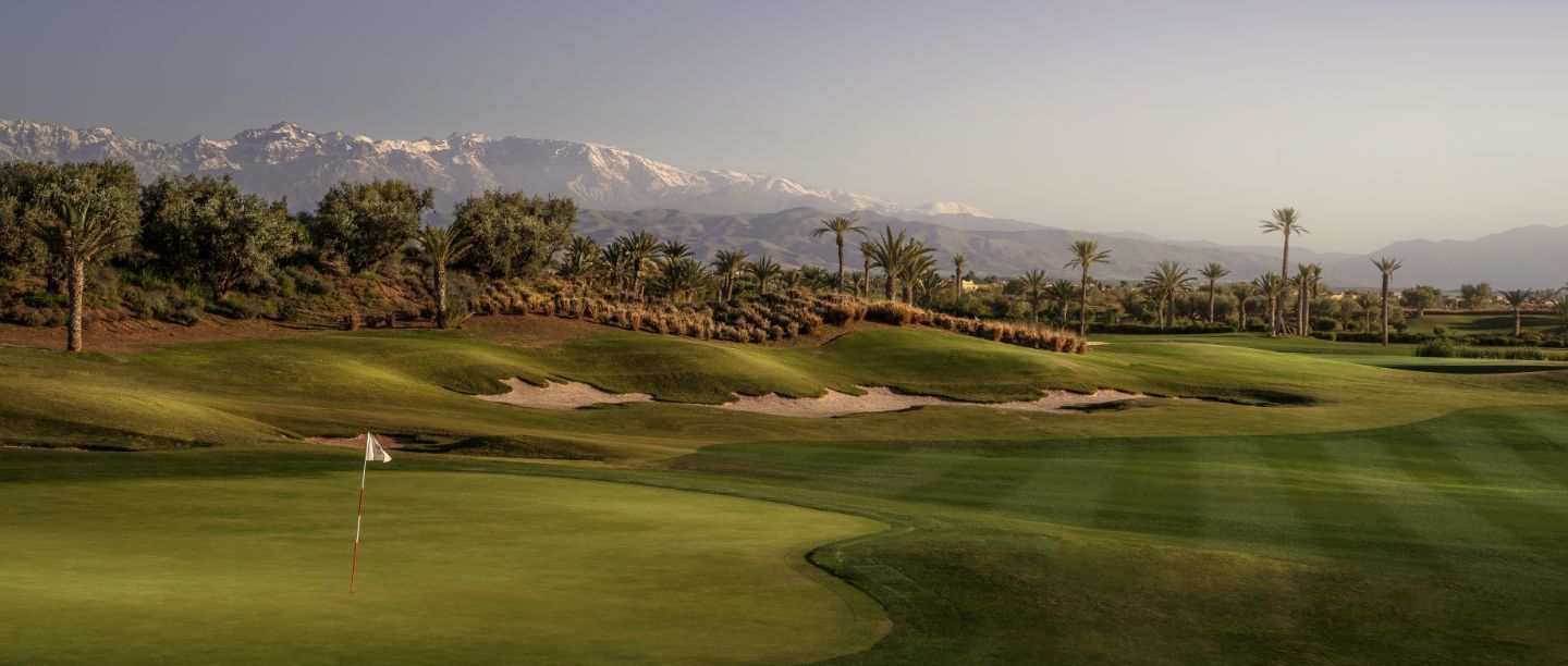 Terrain de golf avec fairways verdoyants, bunkers de sable, palmiers et montagnes à l'horizon