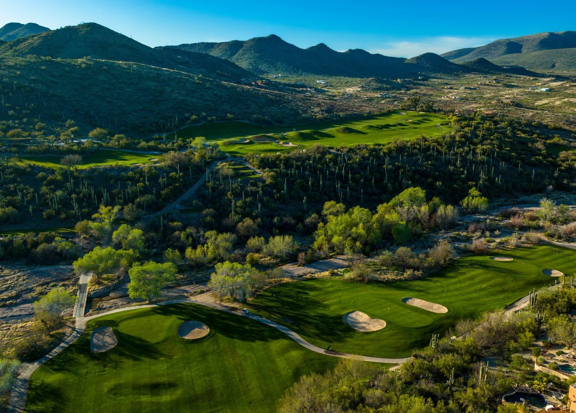Terrain de golf avec fairways verdoyants, bunkers de sable, palmiers et montagnes à l'horizon