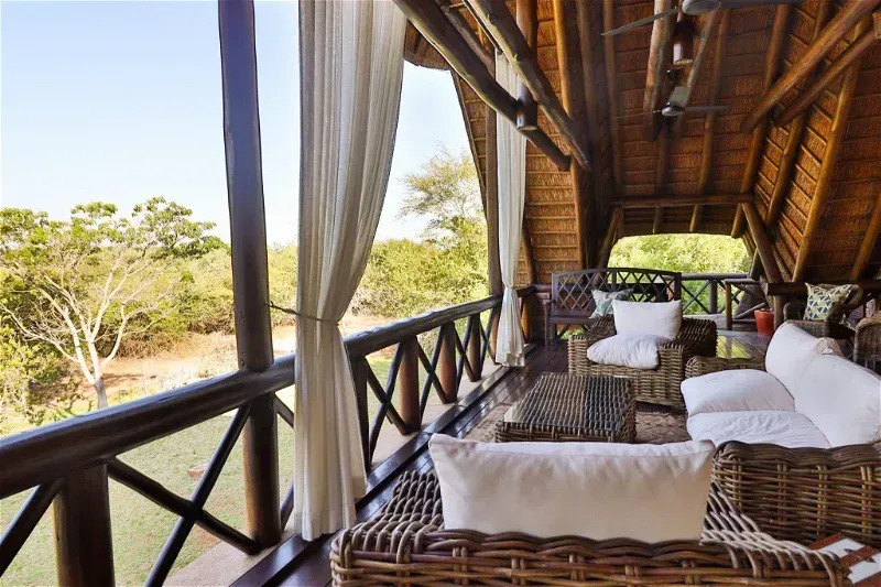 Balcon donnant sur les arbres, avec mobilier en osier et coussins blancs avec vue sur le bush
