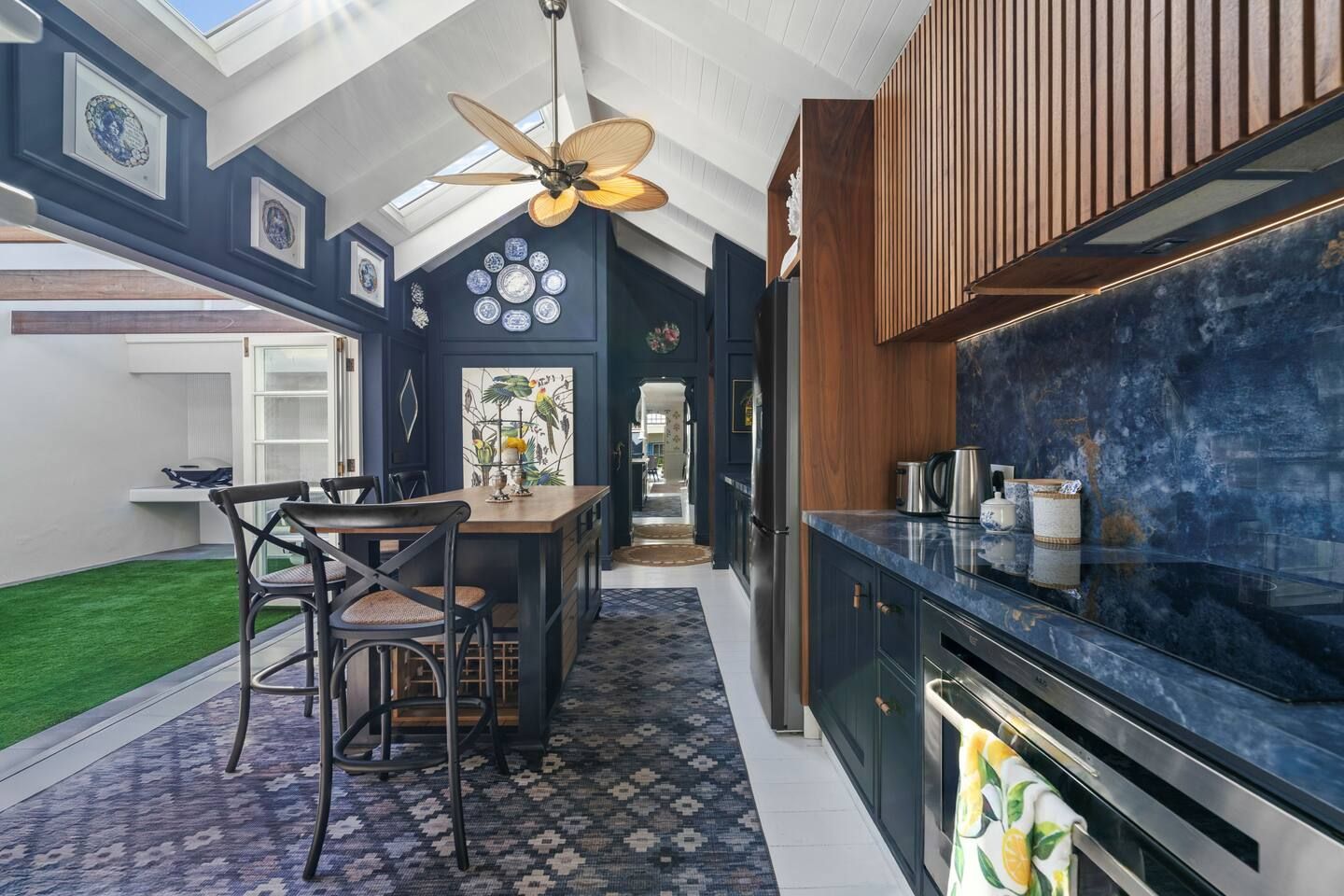 Cuisine et salle à manger modernes avec des meubles sombres, une crédence bleue, des touches de bois