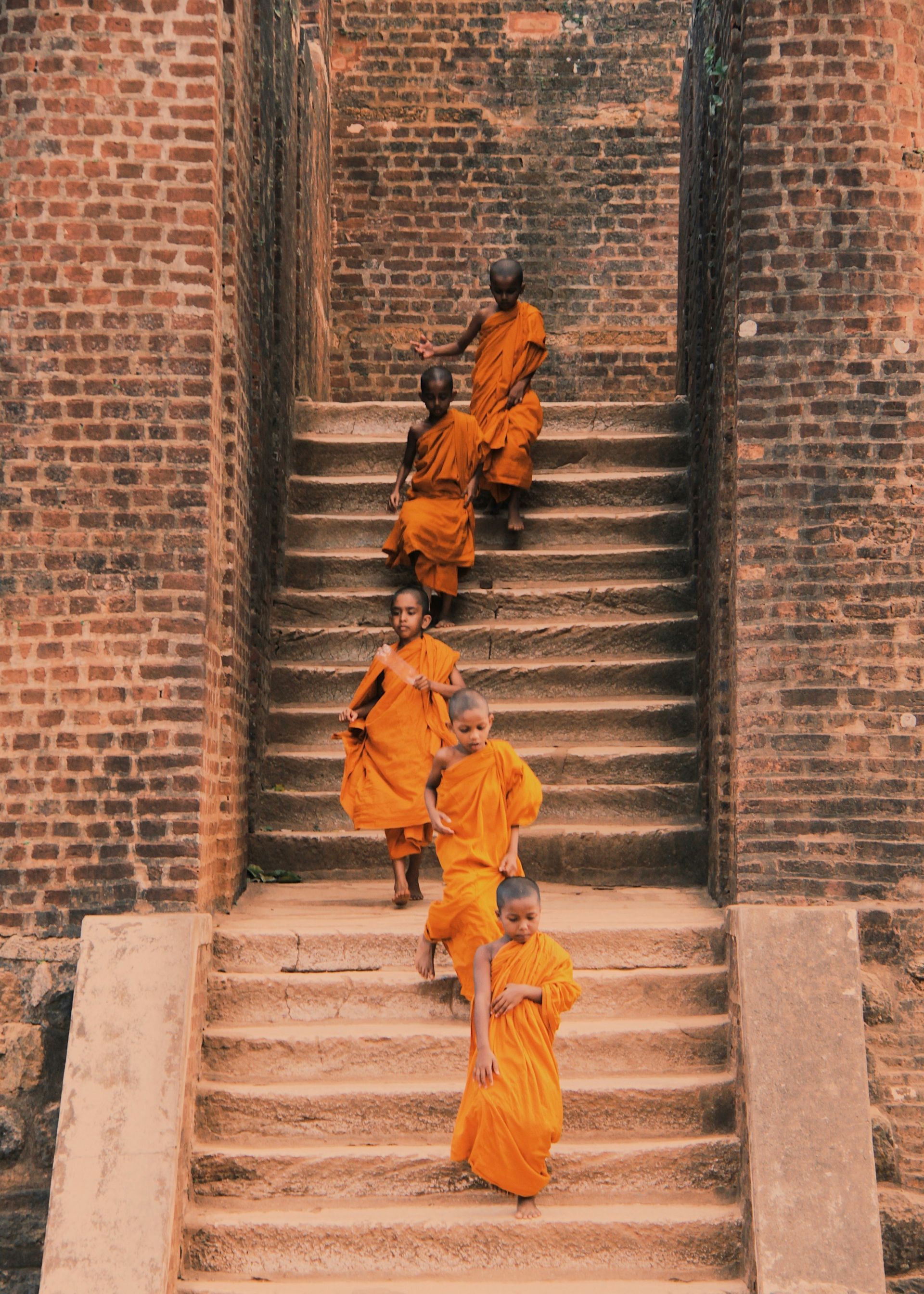 Jeune moine en tenue traditionnelle descendant les marches d’un ancien monastère sri-lankais
