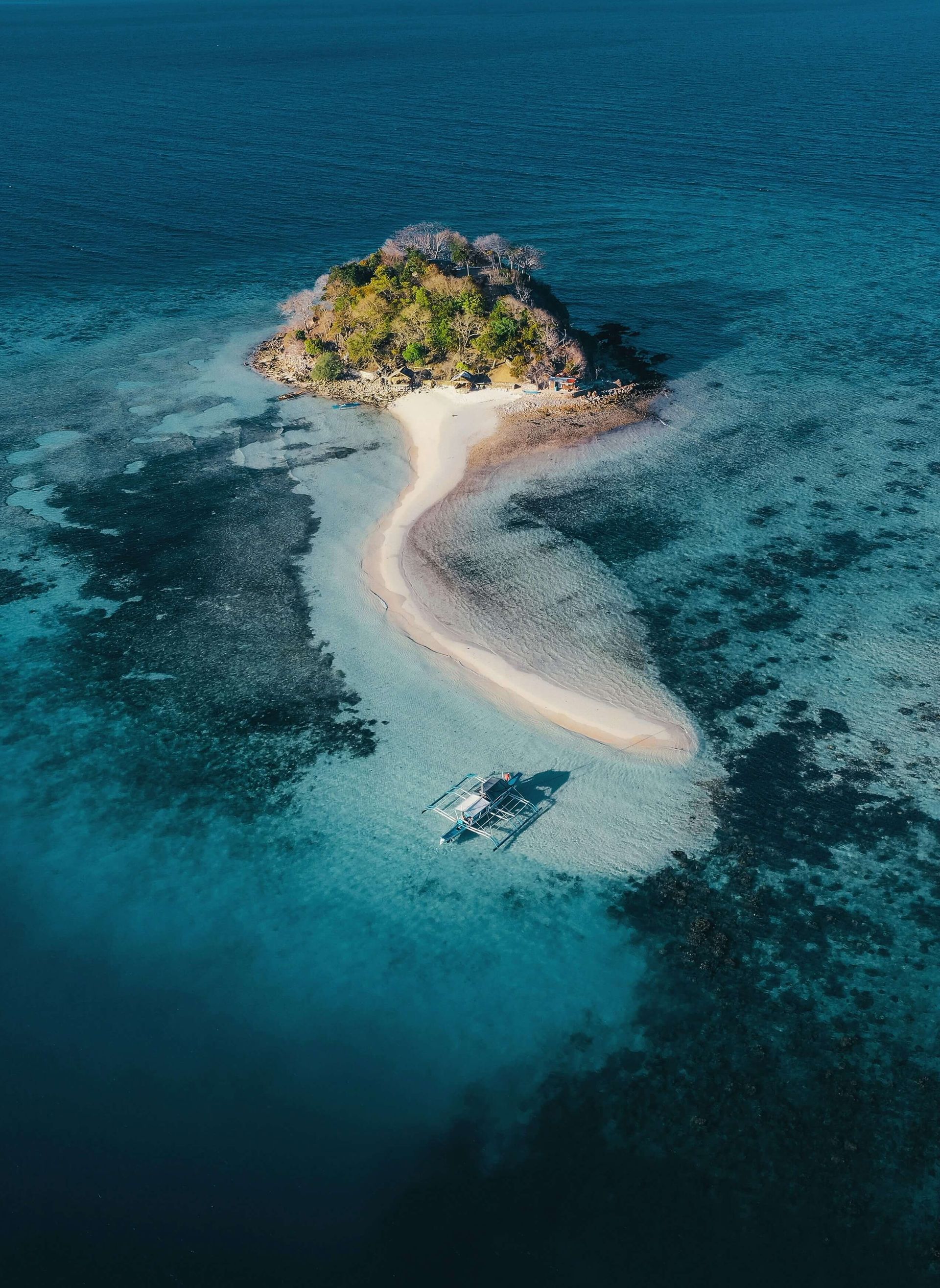 Petite île à la végétation luxuriante, reliée par un sentier sablonneux, entourée d'un océan turquoise et d'un bleu profond.