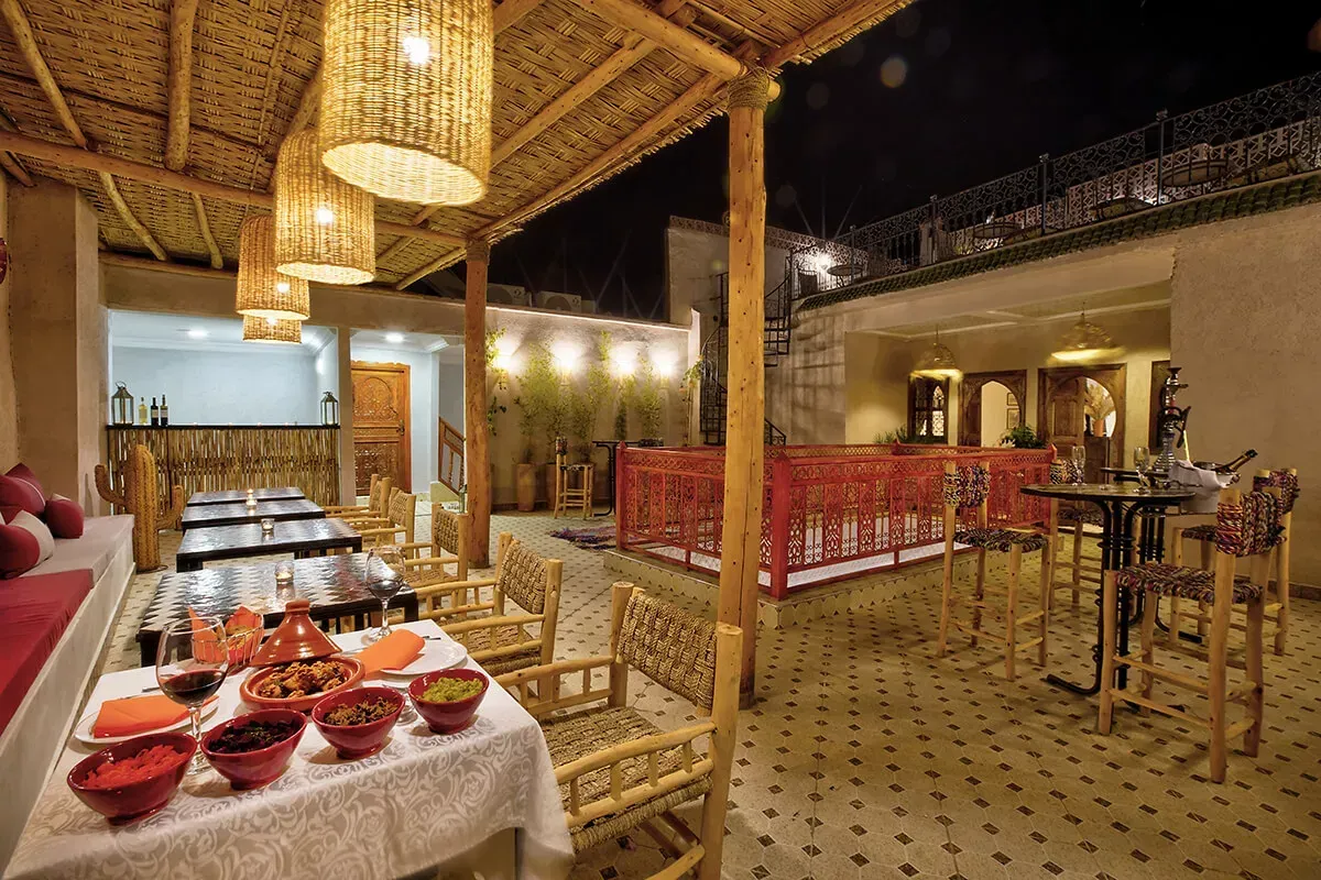 Espace repas extérieur avec lampes en osier, tables avec nourriture et bar.