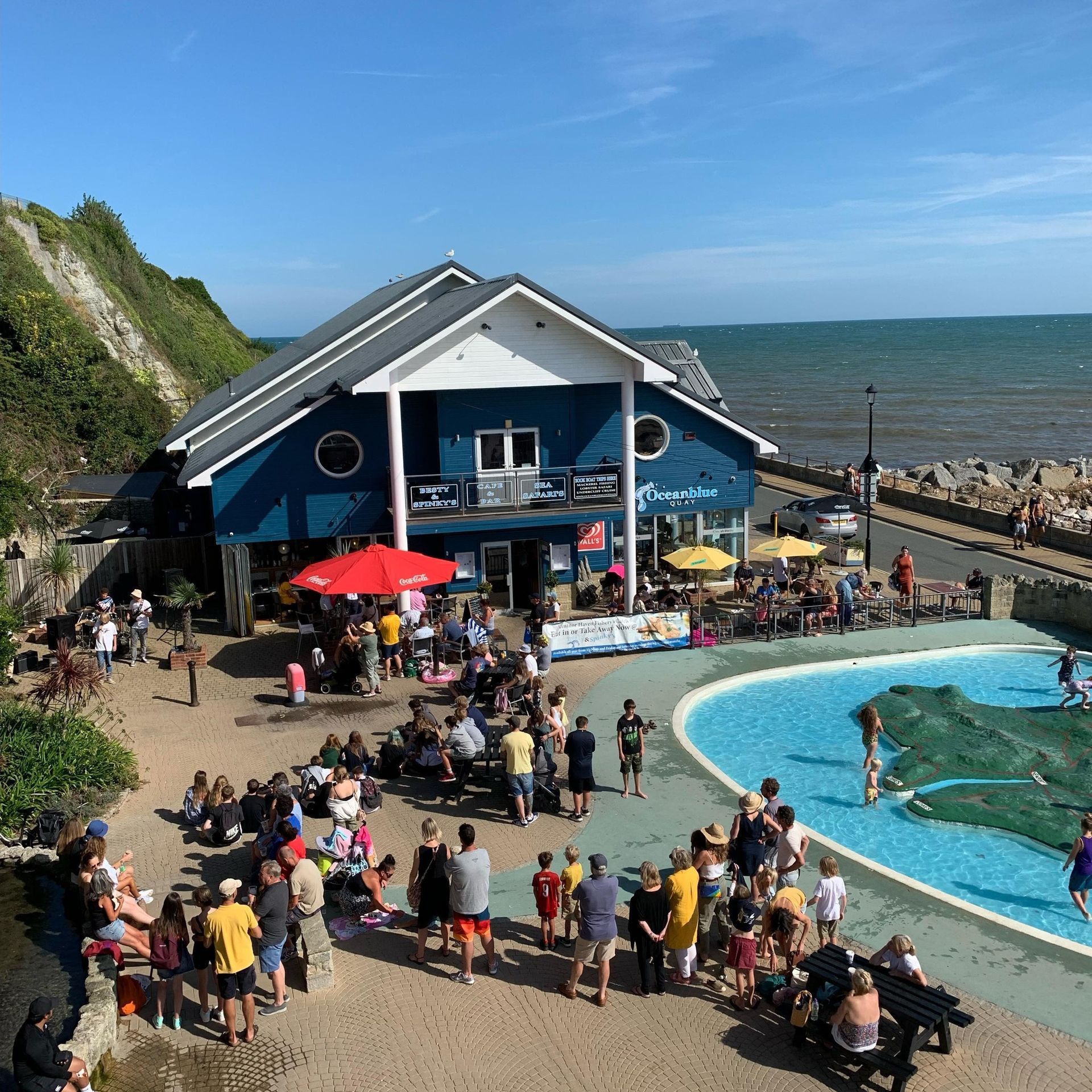 A large group of people are gathered outside of a building next to a swimming pool.