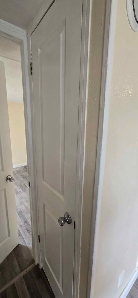 White paneled closet door in a hallway with dark wood flooring and beige walls.