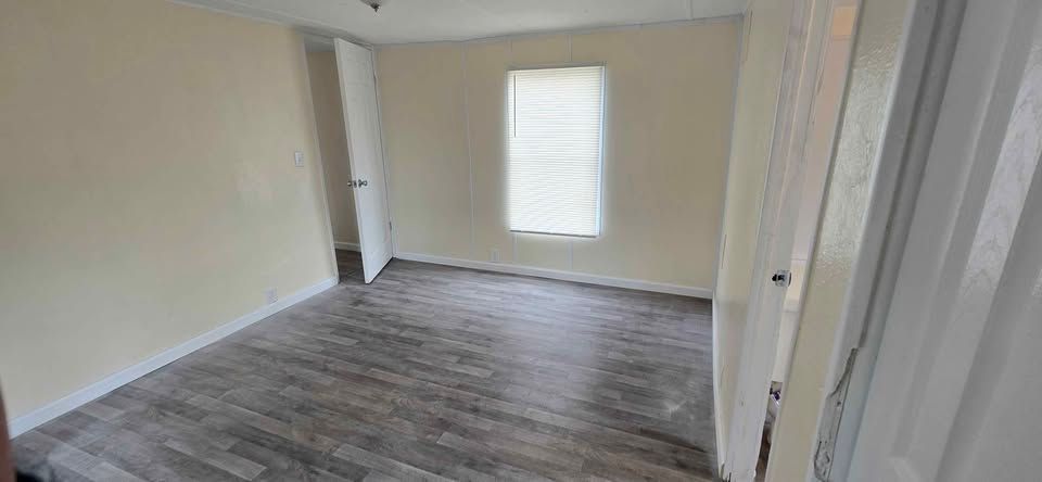 Empty beige room with gray wood-look flooring, a window with blinds, and an open doorway