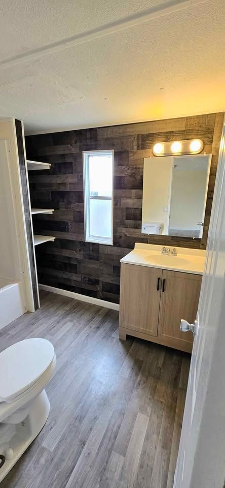 Small bathroom with dark tile shower wall, vanity mirror lights, and gray wood-look floor.