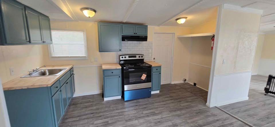 Empty kitchen with blue cabinets, black stove, and wood-look flooring in a bright room