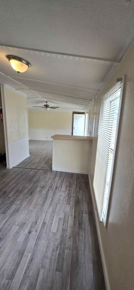 Empty apartment interior with gray wood floors, white walls, and a small kitchen counter.
