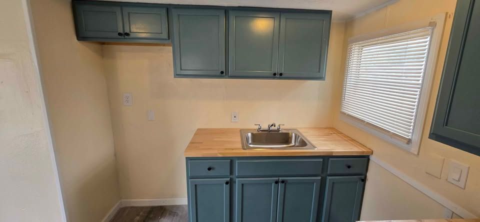 Small kitchen with teal cabinets, sink, countertop, and window blinds
