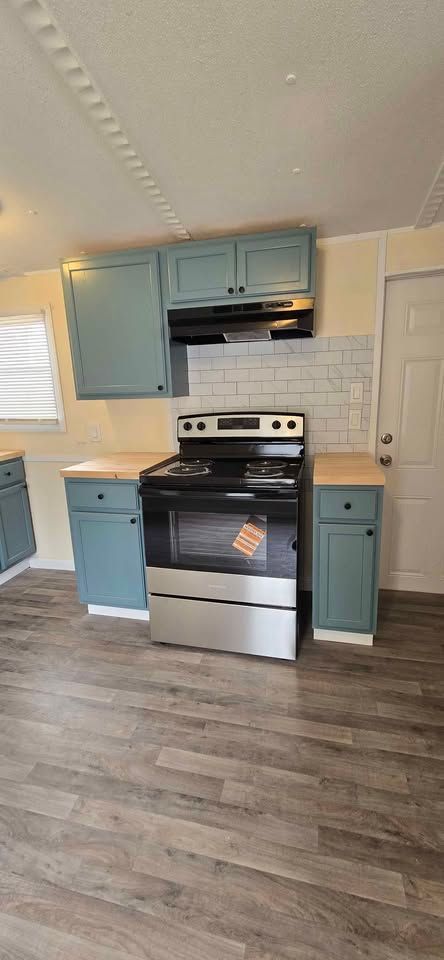 Small kitchen with blue cabinets, stainless stove, white tile backsplash, and wood-look flooring.