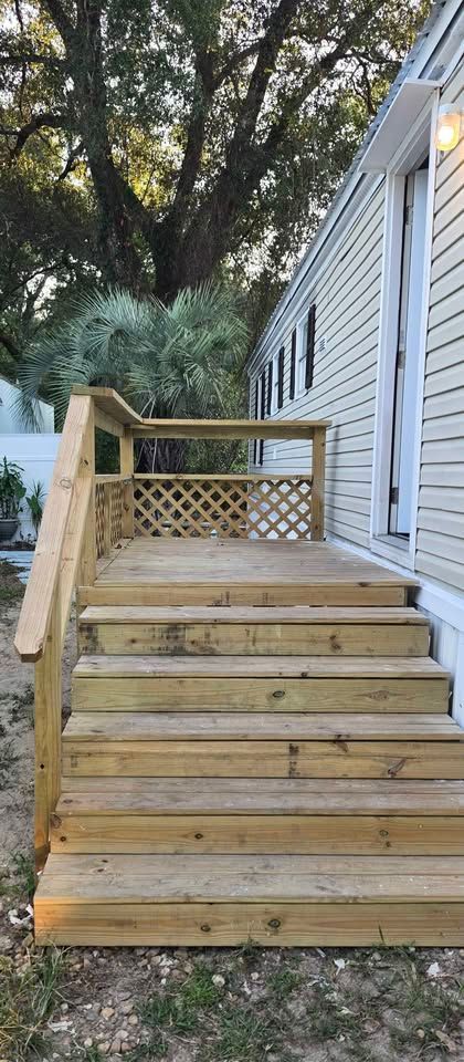 Wooden backyard deck stairs with railings beside a white house and trees