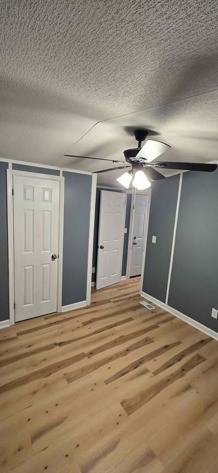 Empty bedroom with gray walls, wood floor, white closet doors, and a ceiling fan light.