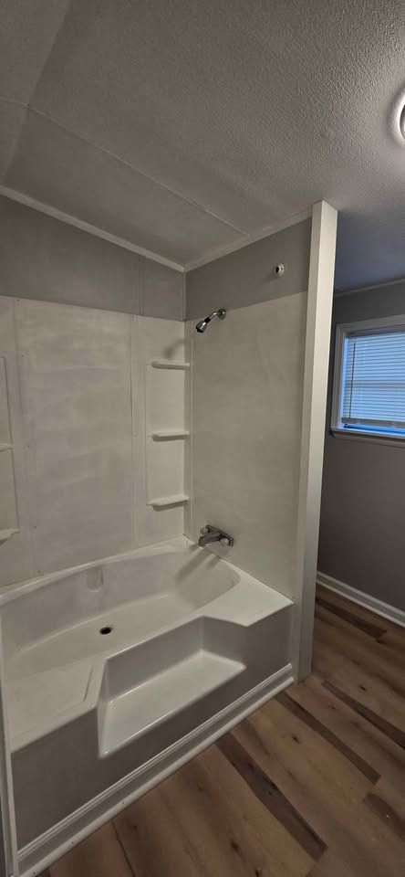 Bright bathroom with a white bathtub, tiled shower walls, and a small window.