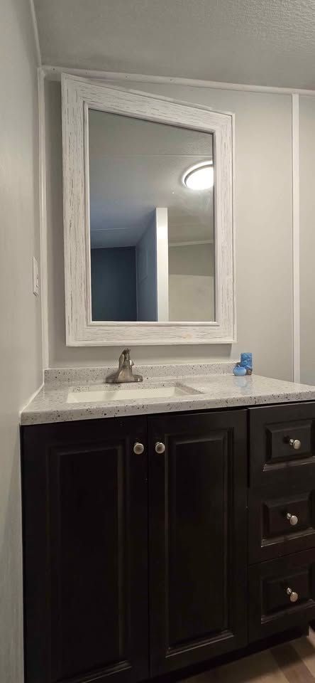 Bathroom vanity with dark cabinets, white countertop, and framed mirror