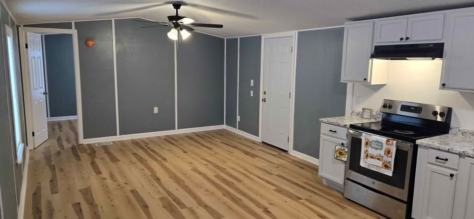 Empty gray living room with hardwood floors and a small kitchen area with stainless steel appliances