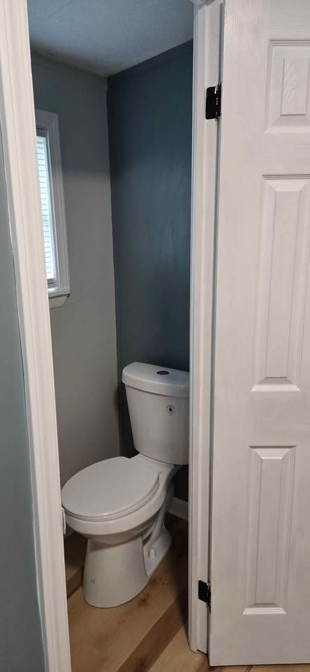 Small bathroom with a white toilet beside an open white door and light blue walls.