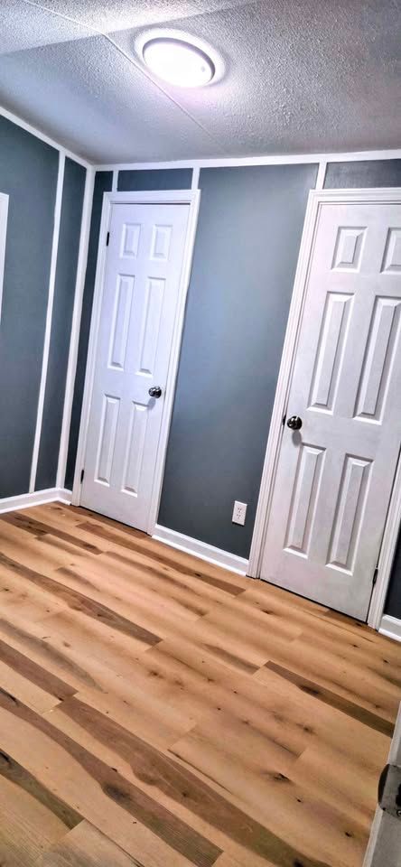Empty room with blue-gray walls, white trim, two white doors, and wood plank flooring.