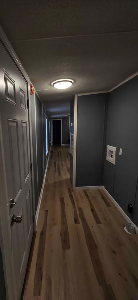 Narrow apartment hallway with gray walls, wood floor, ceiling light, and doors along both sides.