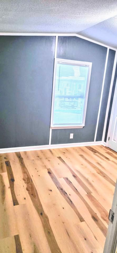 Empty gray room with hardwood floor and a single window on the far wall