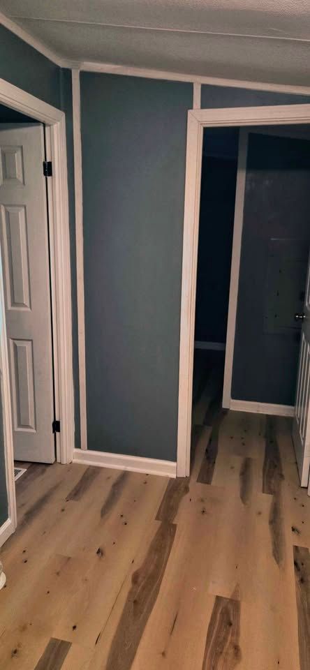 Empty room with teal walls, white trim, wood floor, and an open doorway to a dark hall.