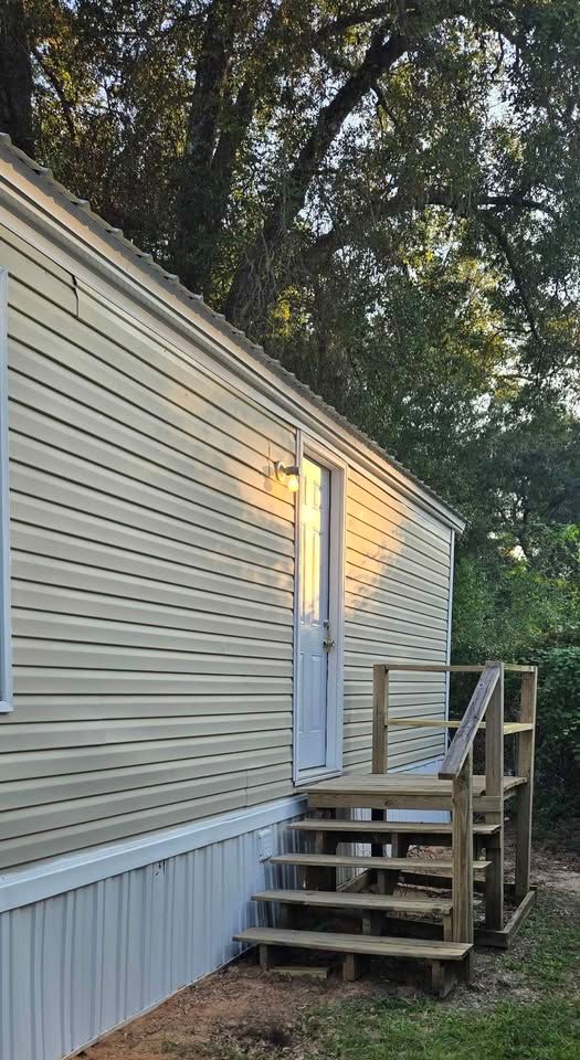 Beige mobile home exterior with a lit door and wooden steps leading up to a small porch.