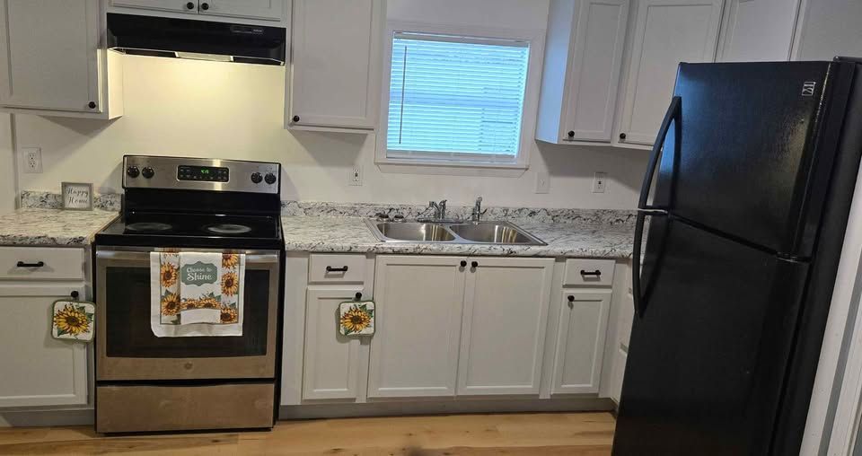 Small white kitchen with black stove and refrigerator, white cabinets, and a window over the sink.