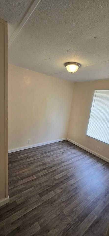 Empty beige bedroom with wood-look flooring, ceiling light, and a window with blinds.