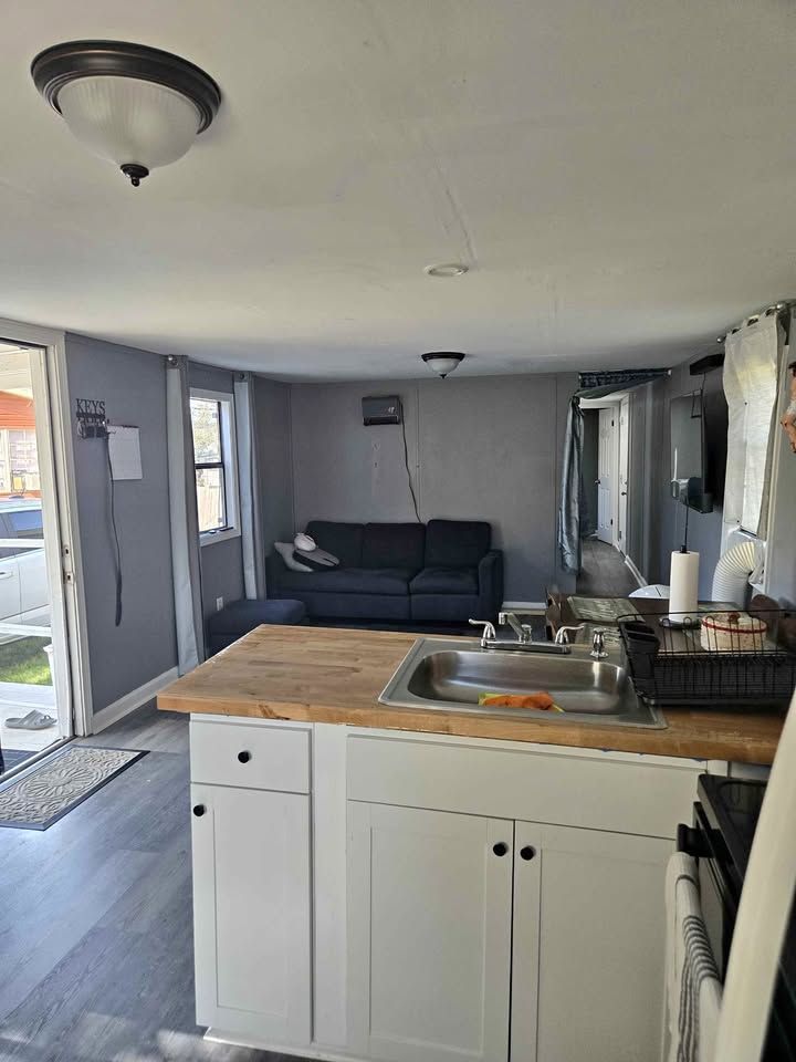 Open-plan kitchen and living room with white cabinets, wood counter, and dark sofa near a sliding glass door