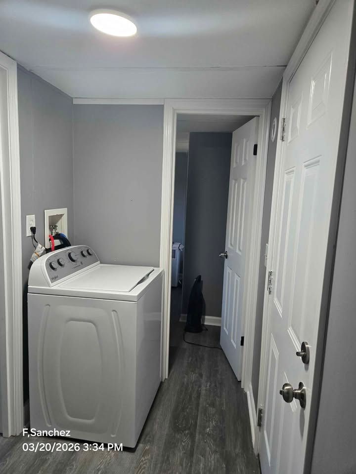 Laundry room with white washer, gray walls, and narrow hallway with white doors.