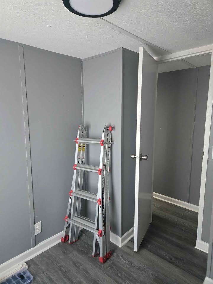 Small gray room with an open door and a folding ladder leaning against the wall.