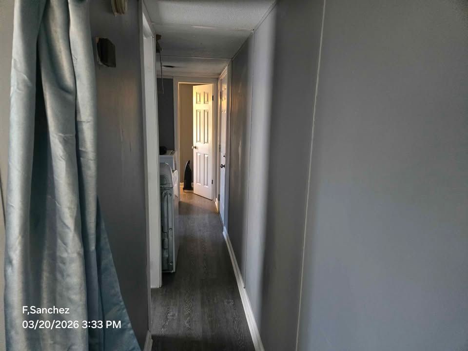 Narrow gray hallway with a lit doorway at the end and a person in the distance