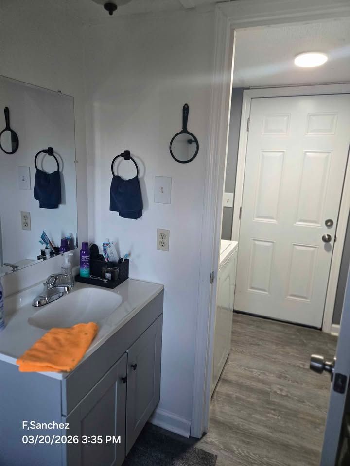 Bathroom vanity with sink and mirror, orange towel, leading to a hallway and front door.